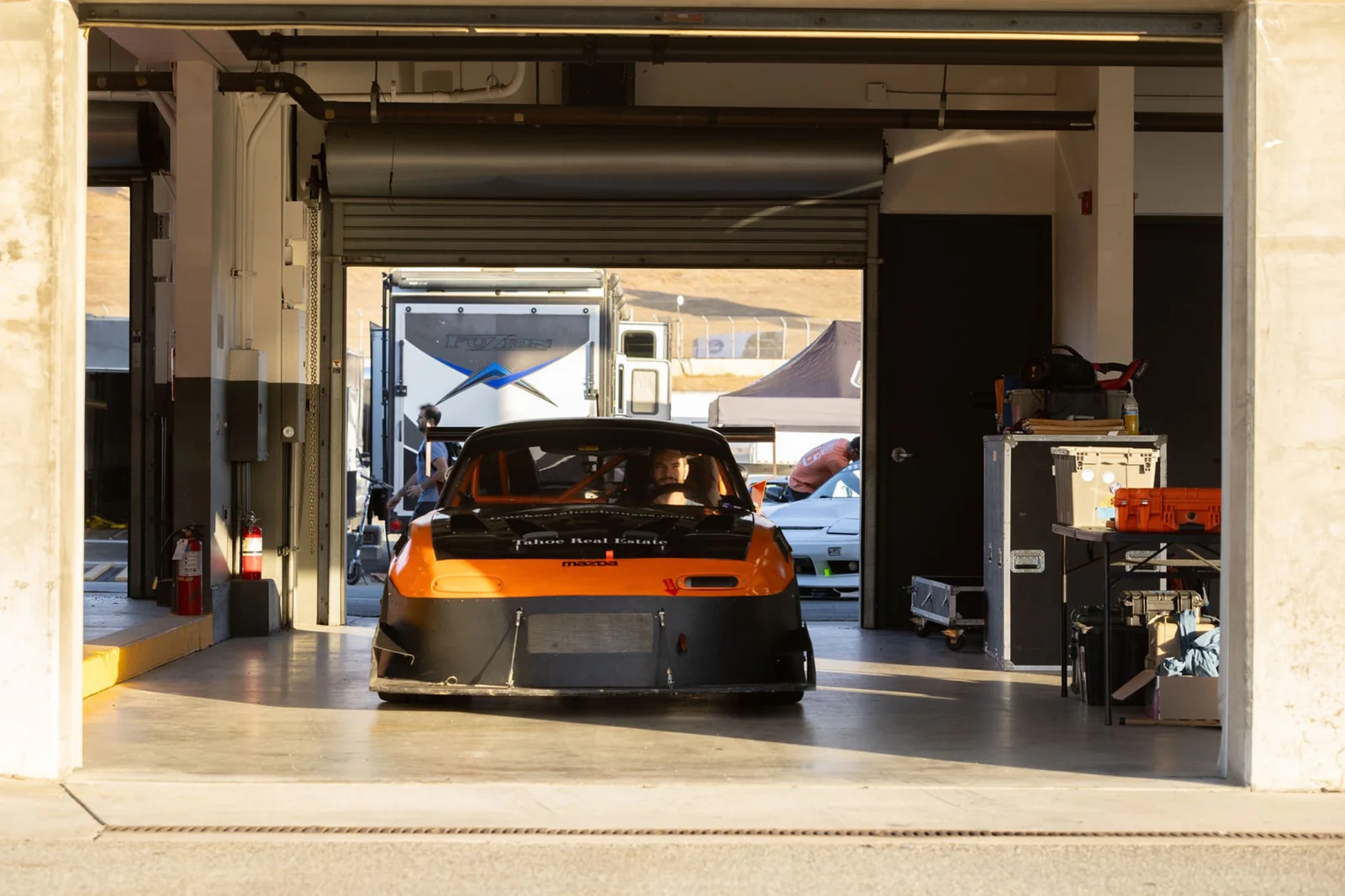 Nick at the wheel of the orange Miata in a sunlit Laguna Seca garage