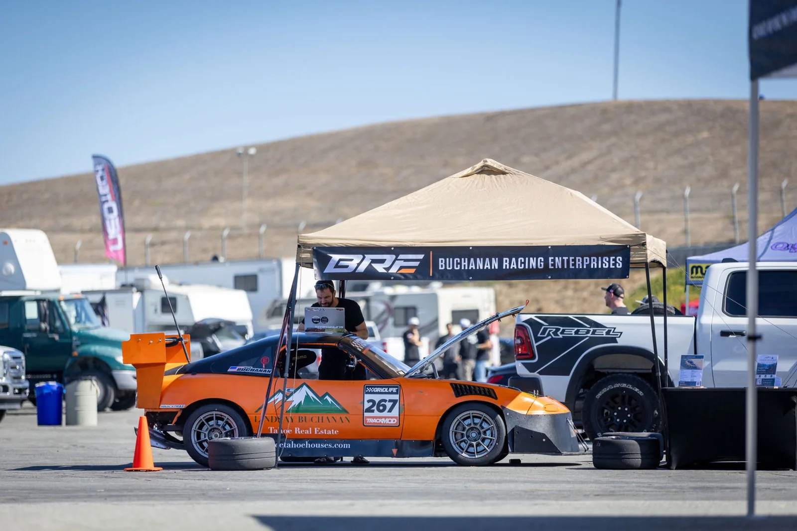 Nick working at a laptop beside the Miata under the Buchanan Racing paddock canopy